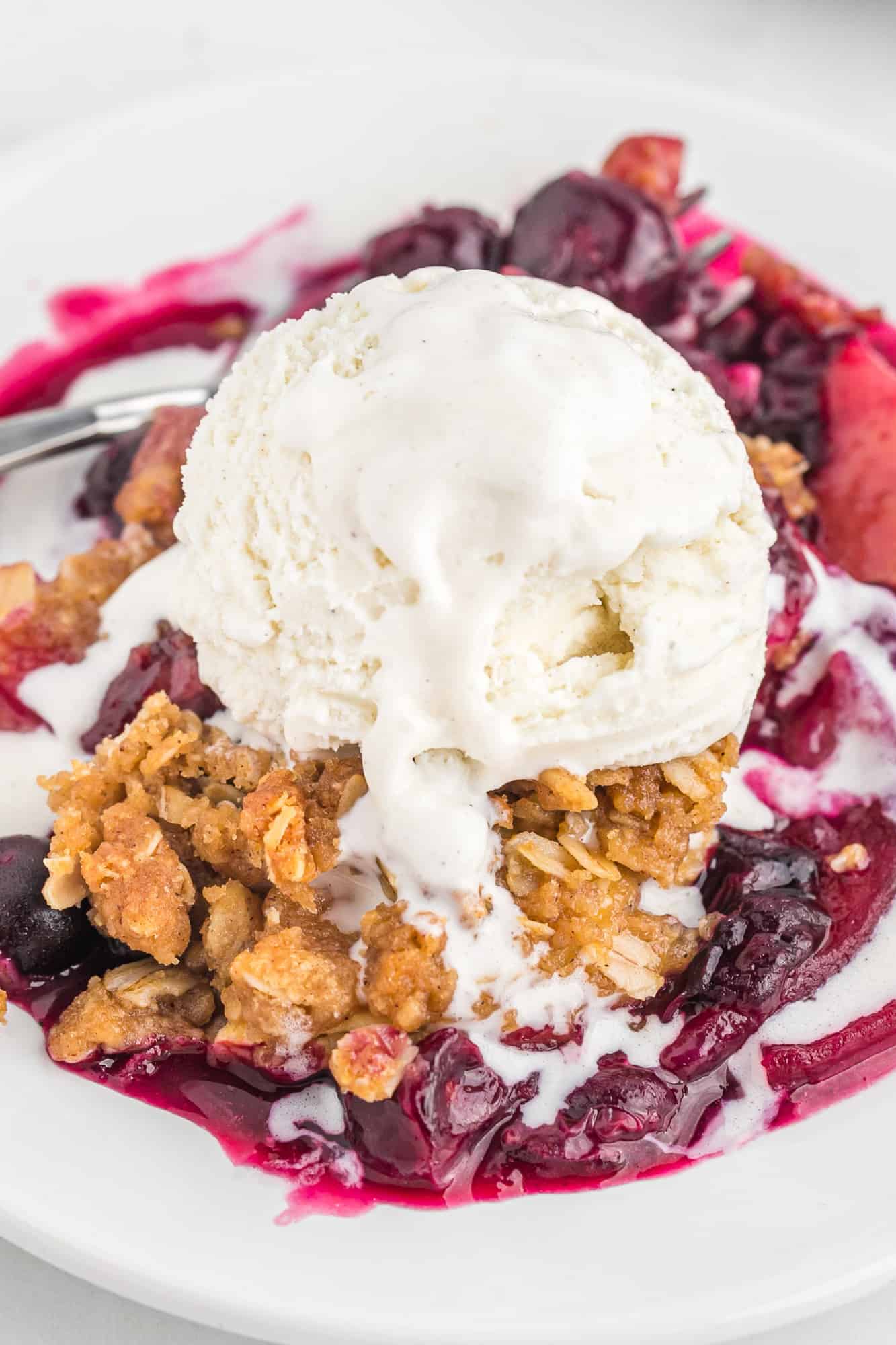 Apple crisp with blueberries and a large scoop of melting ice cream.