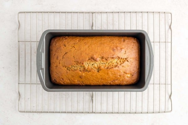 Baked banana bread in a metal loaf pan resting on a wire rack.