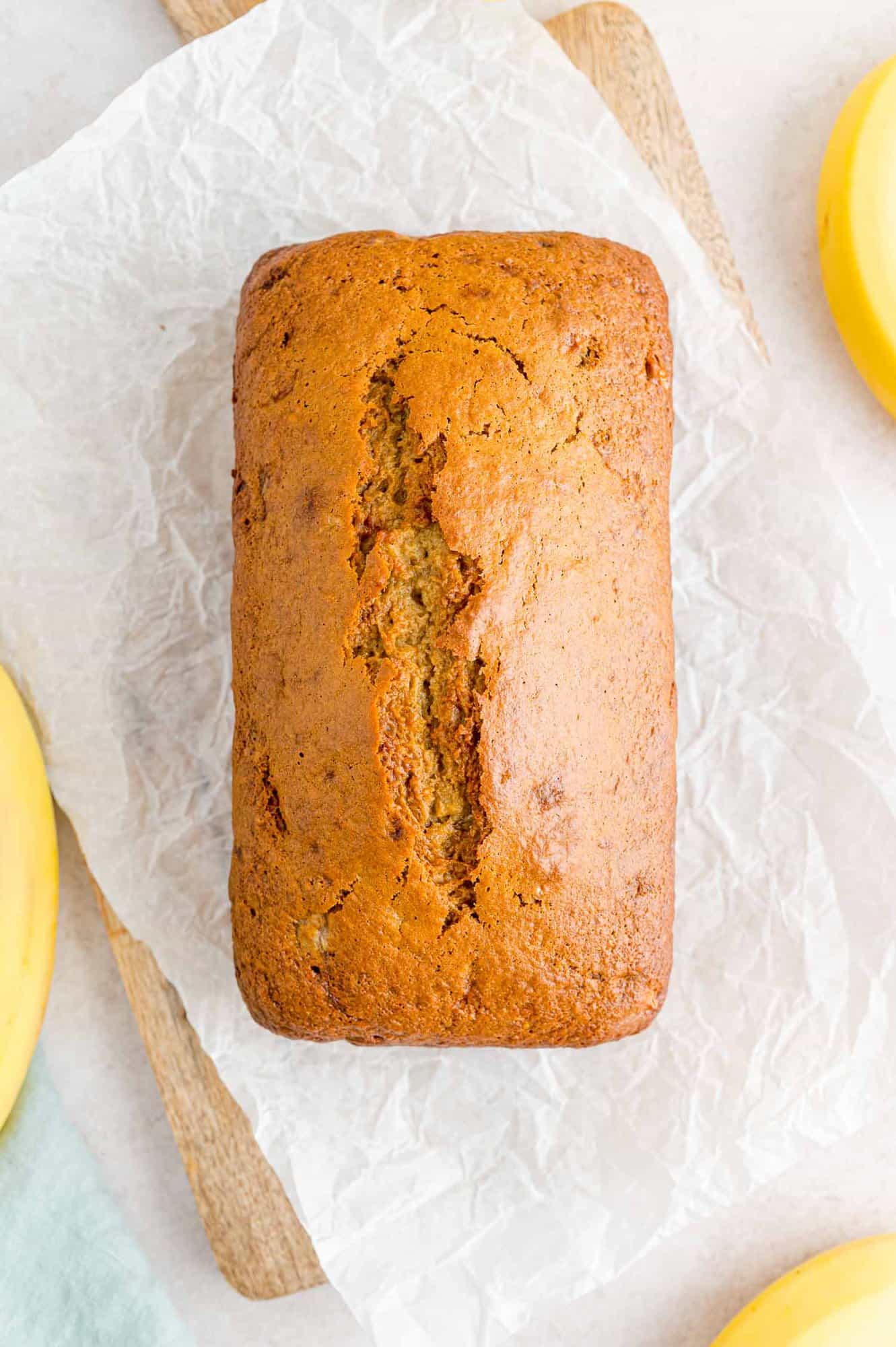 Overhead view of a banana bread loaf on a cutting board lined with a sheet of parchment paper.