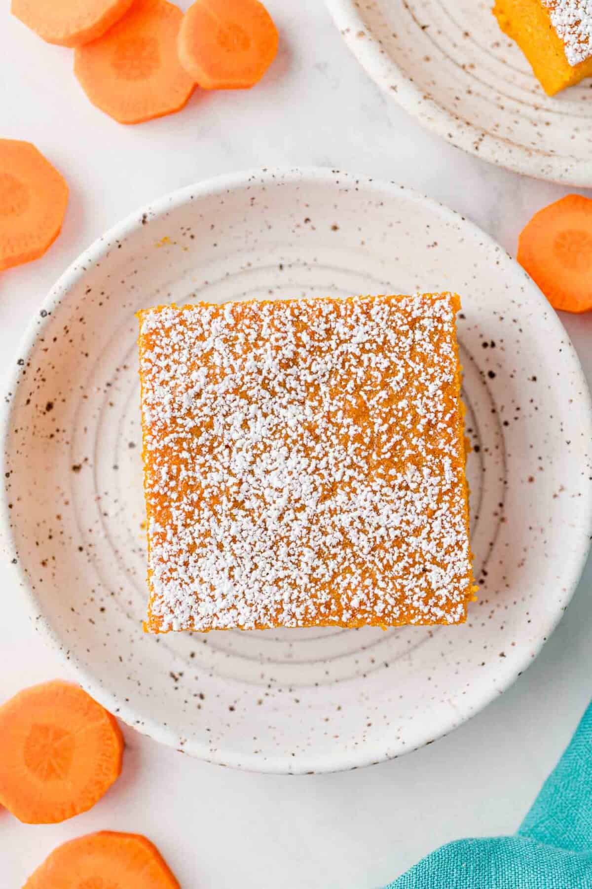 Overhead view of a slice of carrot souffle on a plate, surrounded by carrot slices.