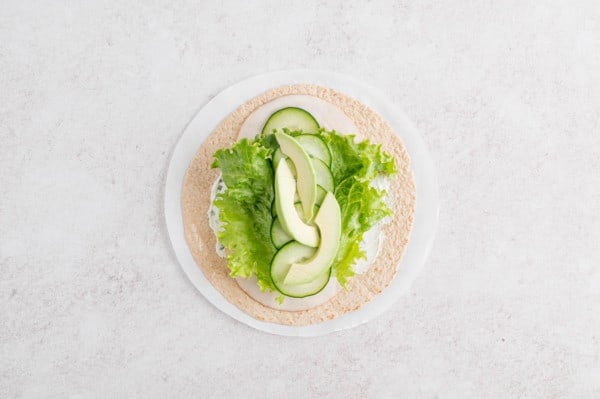 Overhead view of turkey wrap ingredients added to a flour tortilla.