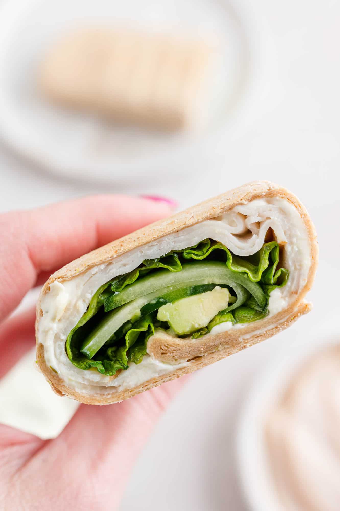 A hand holding up one half of a turkey wrap, with bowls of ingredients in the background.