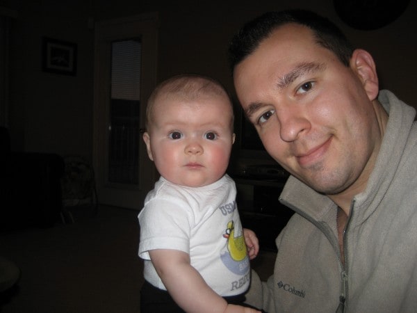 A man and a small baby looking at the camera against a dark background.