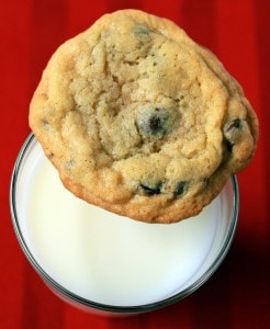 On a red background, top view of a glass of milk, with a cookie balanced on the edge of the glass.