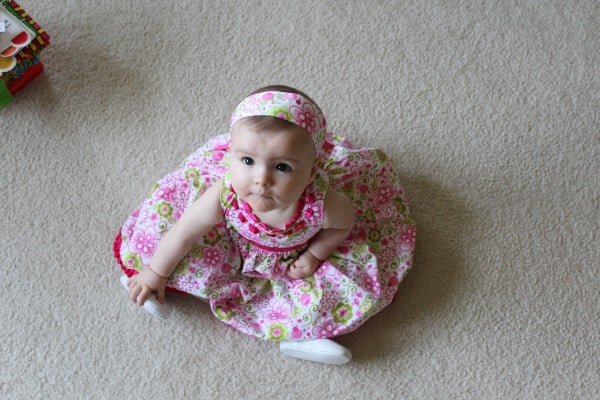 Sweet little girl in a pink dress sitting on white carpet and looking up at the camera.