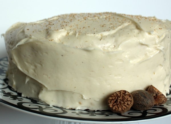 Front view of whole layer cake on white platter with black pattern, garnished by whole nutmeg.