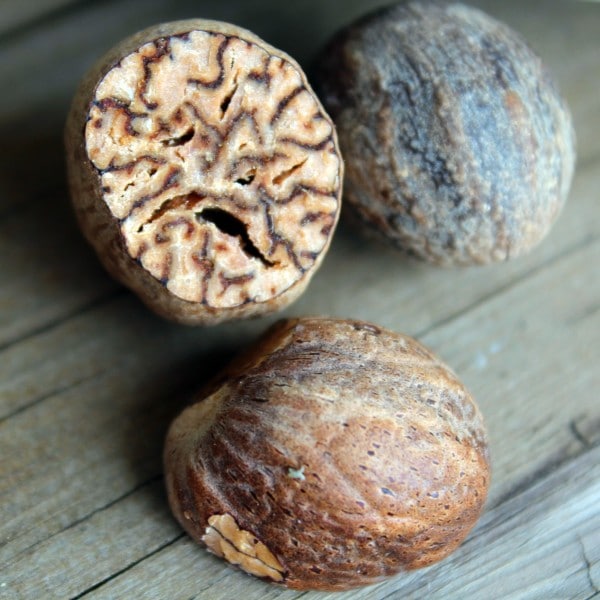 Close up Image of one whole nutmeg, and one sliced in half, showing the inside. Background is wooden deck.
