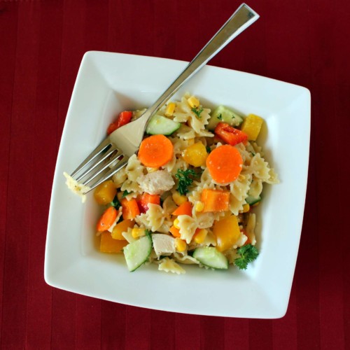Close up view of pasta salad with farfalle pasta and carrots, corn, cucumber, chicken, and parsley.