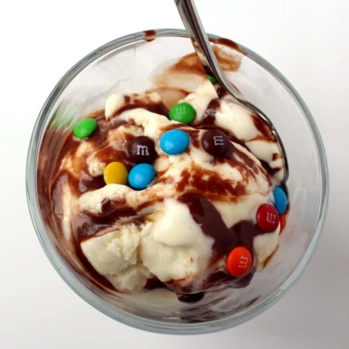 Overhead view of clear glass bowl with ice cream, hot fudge, and M&Ms sprinkled on top.