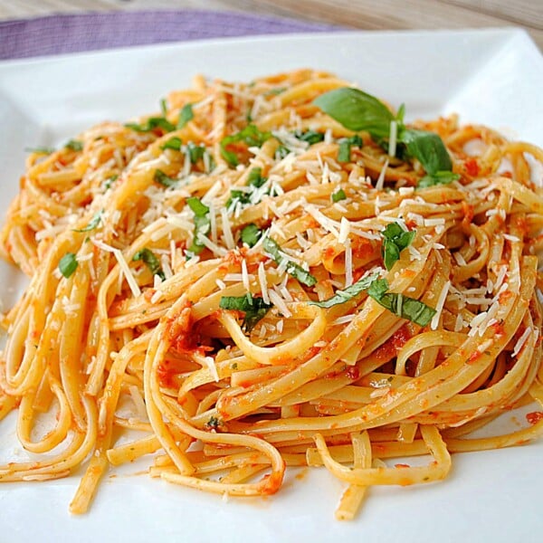 Closeup of linguine in square white plate, garnished with fresh basil.