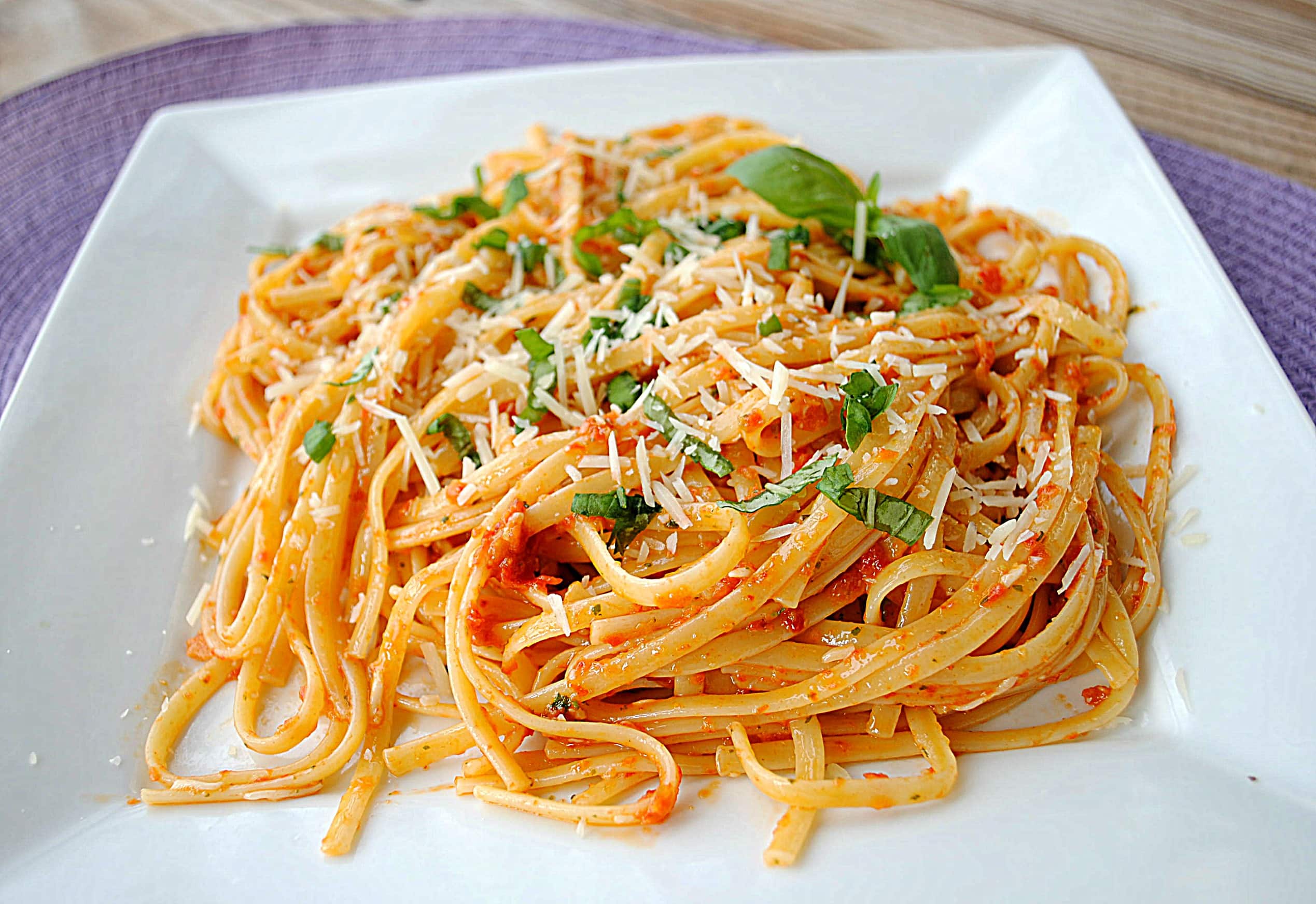 Closeup of linguine in square white plate, garnished with fresh basil.