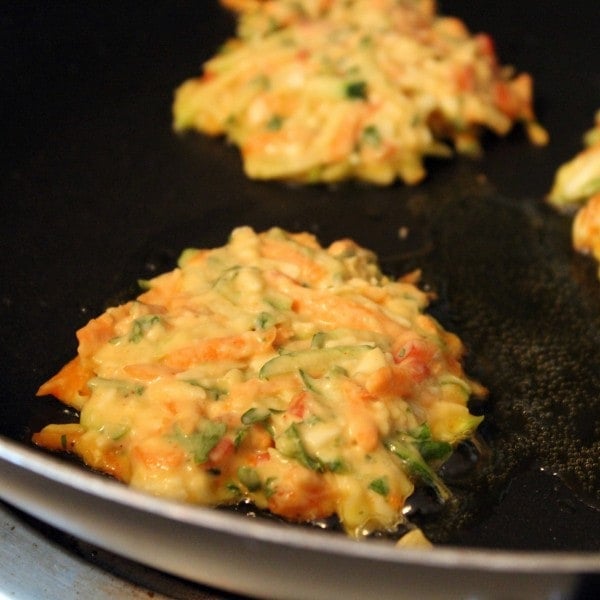 Uncooked zucchini and carrot pancakes in a frying pan cooking.