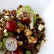 Close up view of lentils, red grapes, celery, walnuts, and feta. A shiny dressing is also visible.