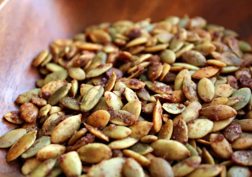 Close up of a large pile of seasoned roasted pepitas in varnished wooden bowl.