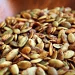 Close up of toasted pepitas in a wooden bowl.