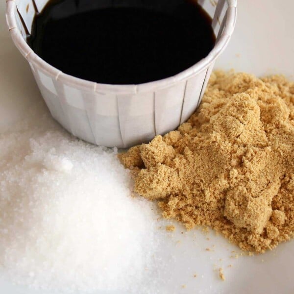 Overhead view of small paper cup containing soy sauce, surrounded by small mounds of white sugar and ground ginger.