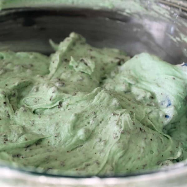 Large metal bowl of mint green frosting with chocolate bits in it.