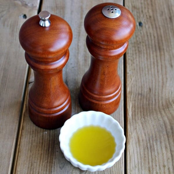 Overhead view of wooden salt and pepper grinders, with small dish of olive oil, on deck boards.