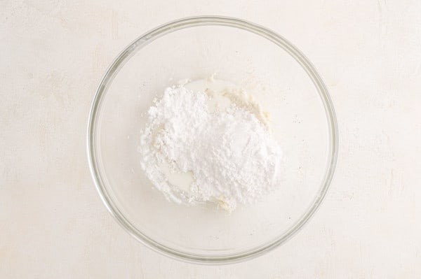 Powdered sugar added to a glass mixing bowl with butter, cream, and vanilla.