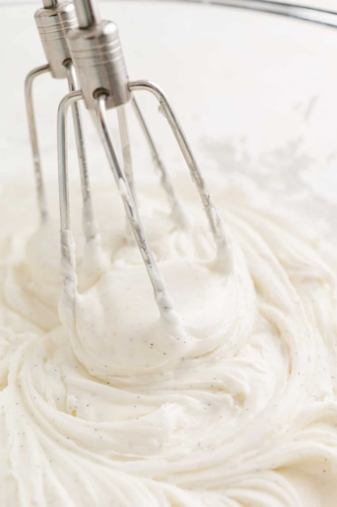 Two electric mixer attachments in a bowl of vanilla buttercream frosting.