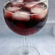 Stemmed wine glass containing cherry spritzer with ice cubes.