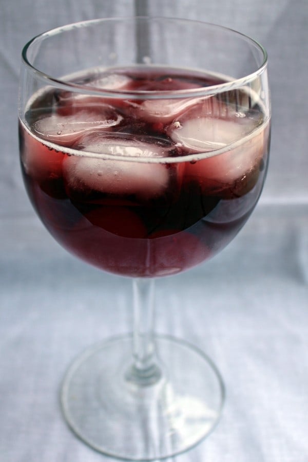 Front view of stemmed wine glass containing wine and cherry spritzer.