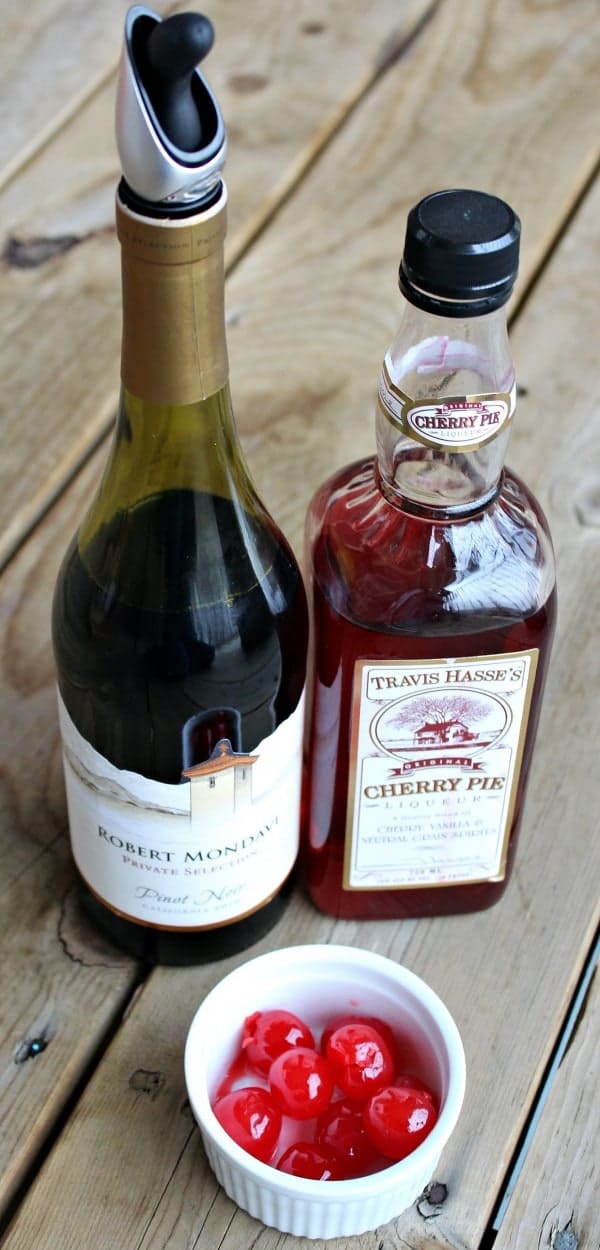 Overhead front view of Robert Mondavi pinot noir wine, a bottle of cherry pie liqueur, and a small white bowl of maraschino cherries