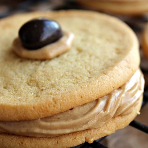 Close up view of a sugar cookie sandwich with brown frosting and topped with a chocolate covered espresso bean.