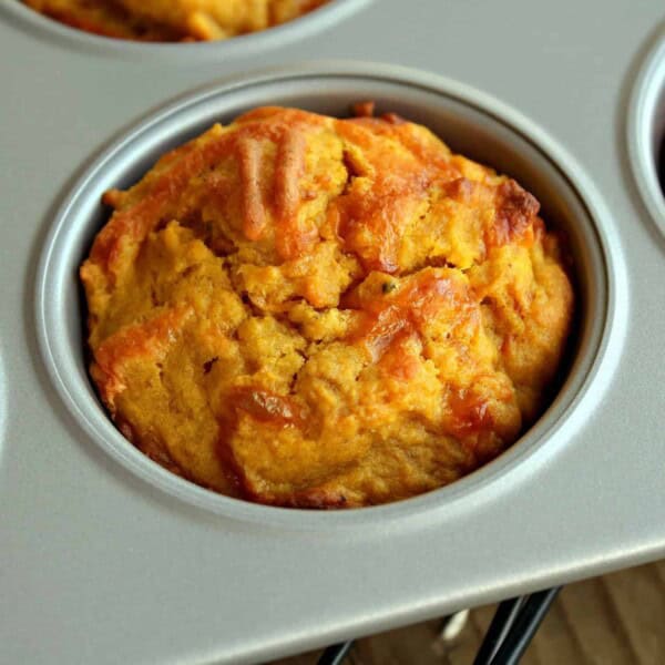 Close up view of a pumpkin muffin in a tin. Cheddar and black pepper are visible in the muffin.
