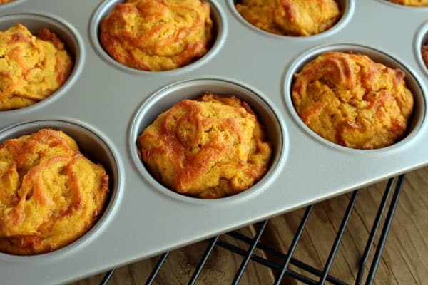 Dark orange muffins in a muffin tin, flecked with shredded cheddar cheese. 