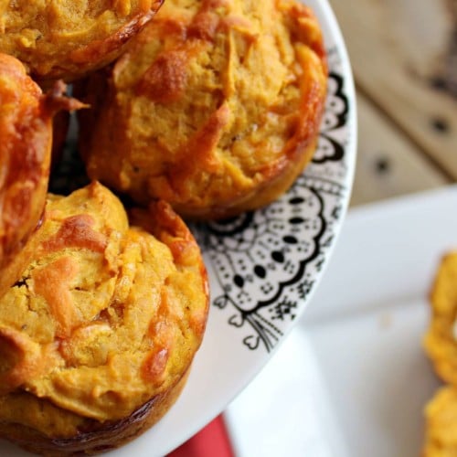 Overhead close up view of muffins on a cake stand, an open muffin with butter on a white plate sits below in the background.