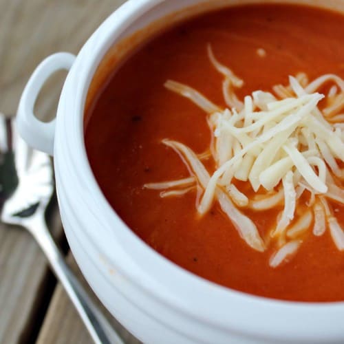 Tomato soup in a white bowl, sprinkled with cheese.