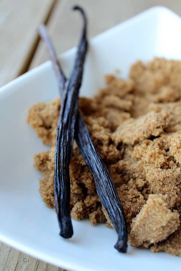 Closeup of two vanilla beans in a bowl with dark brown sugar.