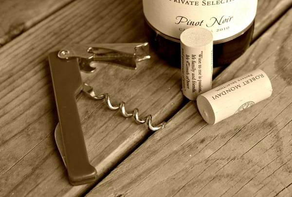 Close up of metal cork screw, two corks and partial image of wine bottle on wooden deck boards.