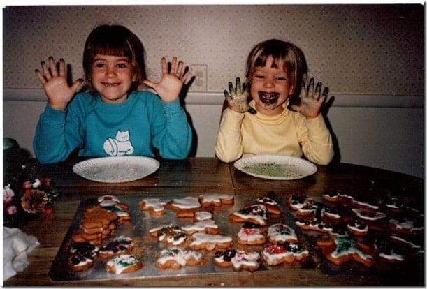 Two young girls with messy hands and faces, in the process of decorating cookies.