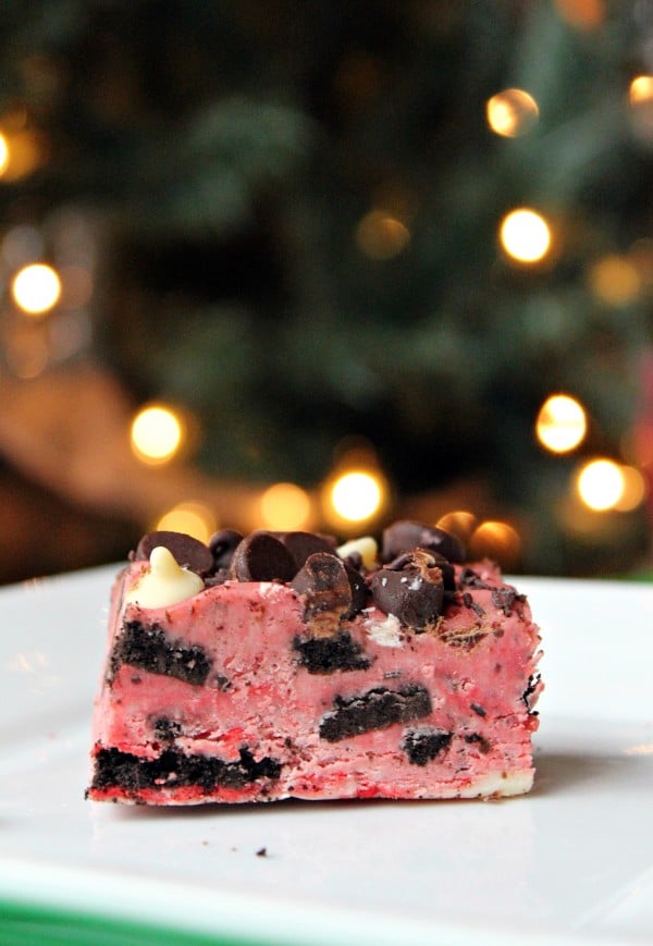 A of pink fudge flecked with cookies and cream pieces, as well as chocolate chips and white chocolate chips. A holiday tree is visible in the background.