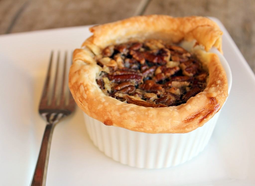 One pecan pie in a ramekin, with fork, on square white plate.