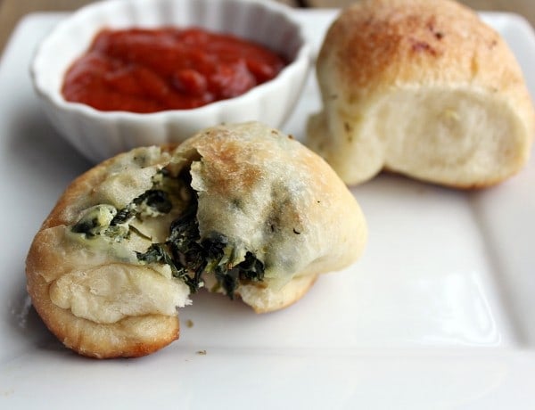 Two pizza bites on square white plate, one intact and one broken open, with bowl of sauce in background.