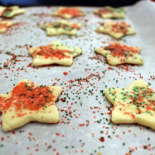 Cut out cookies in the shape of stars sprinkled with red and green sugar on cookie sheet.