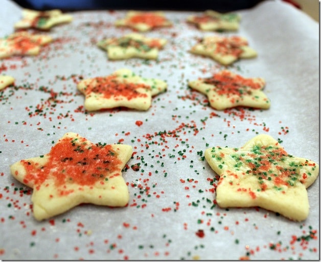 Front view of cut out sugar cookies in star shape with red and green colored sugar on parchment lined cookie sheet.
