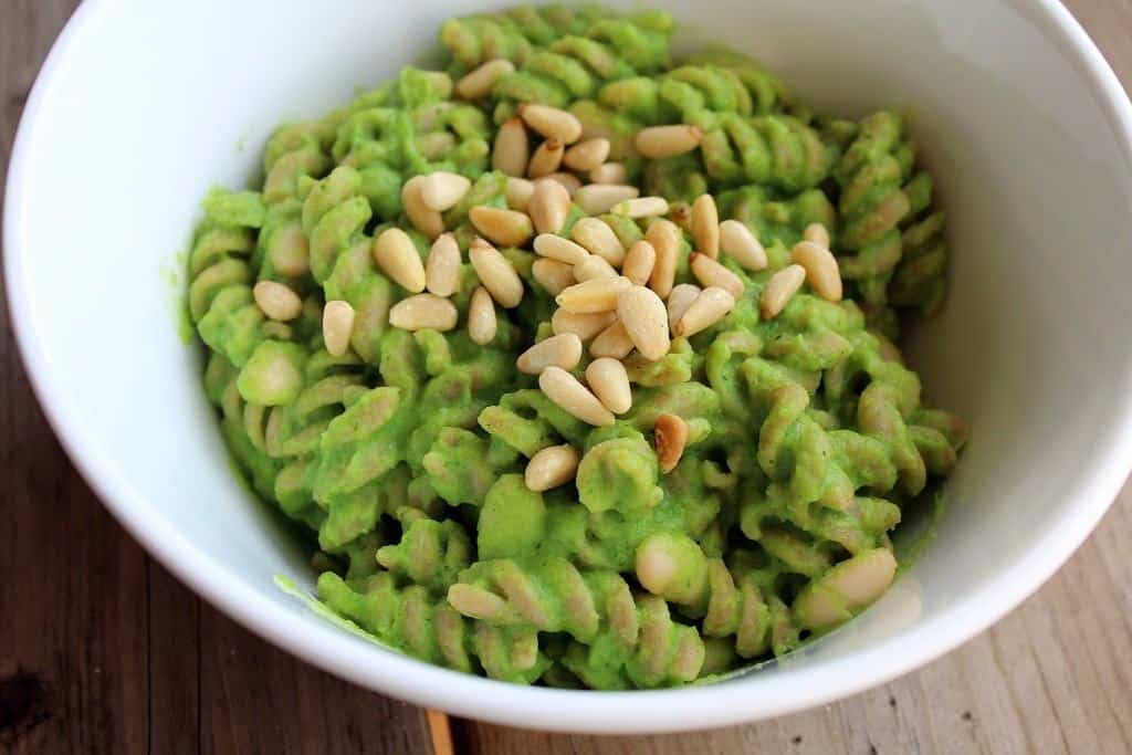 Round white bowl containing pasta with broccoli pesto, garnished with pine nuts.