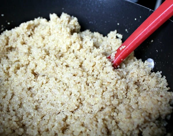 Closeup of cooked quinoa in pan, with red spoon inserted.