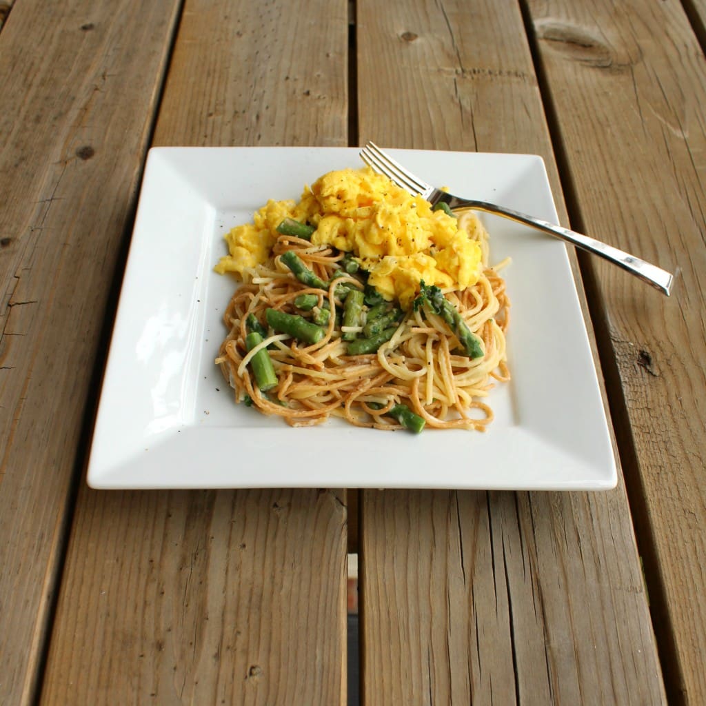 Square white plate containing a serving of pasta with asparagus and scrambled eggs.