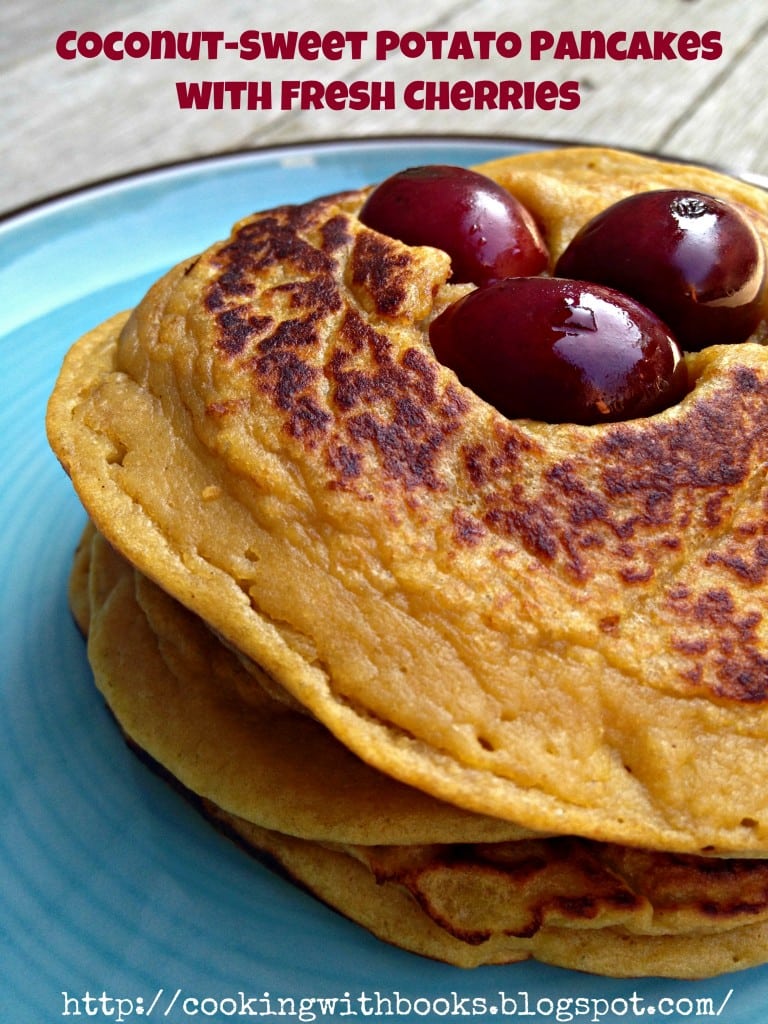 Closeup partial of stacked pancakes topped with three black cherries on blue plate with text overlay "coconut-sweet potato pancakes with fresh cherries."