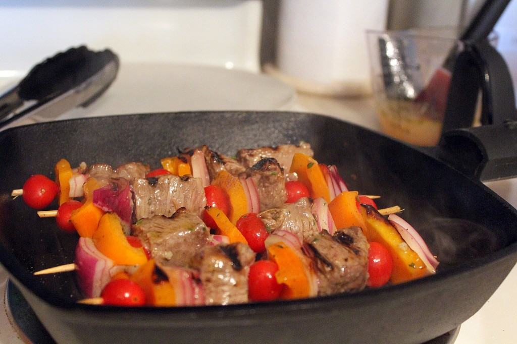 Several kebabs in grill pan on stove.