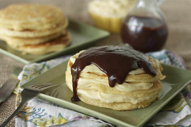 Pancakes on plate with cream and ganache, with plain pancakes in background and pitcher of ganache.