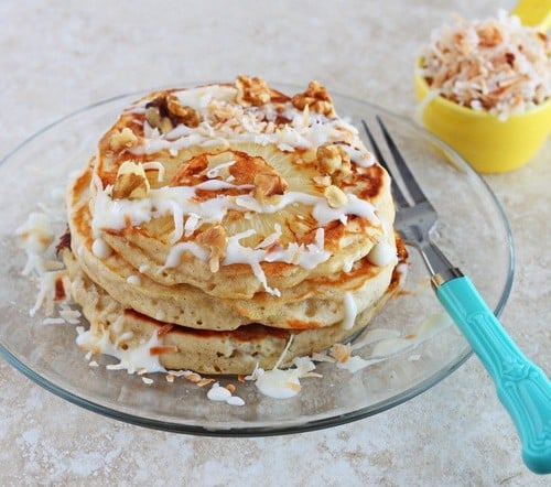 Stack of pancakes with glaze and coconut, on clear glass plate with decorative fork.