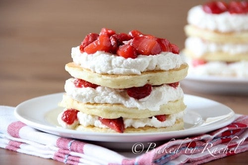 Front shot of 3 pancakes stacked and layered with whipped cream and strawberries.