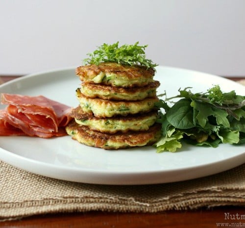 Front view of white plate containing pancakes, dressing, greens, and meat.