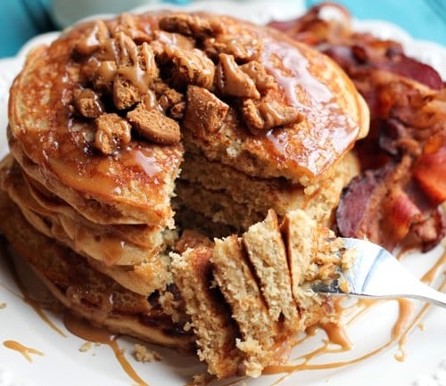 Stack of pancakes with bite removed, accompanied by bacon.